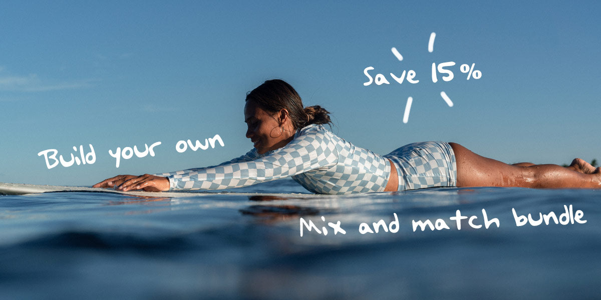 longboard ikit agudo smiling and laying down on her surfboard wearing a blue check surf set