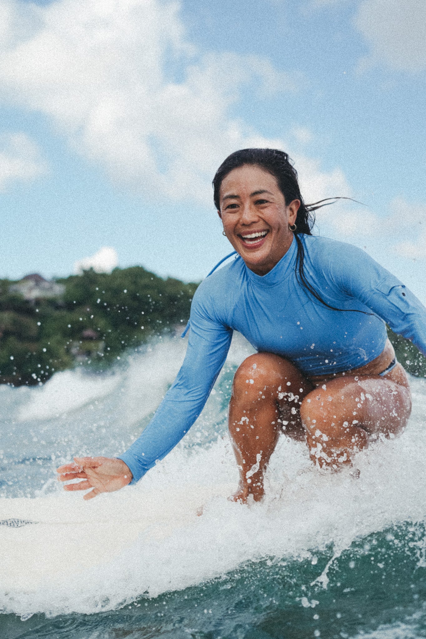 woman smiling and surfing wearing the putu turtleneck top in blue