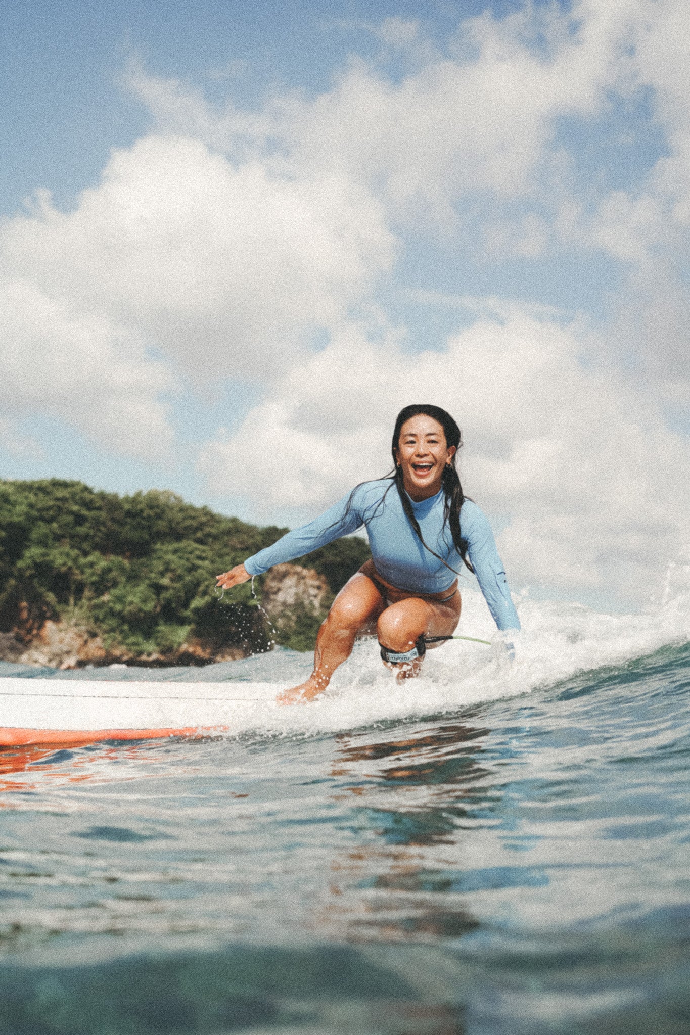 woman smiling and surfing wearing the putu turtleneck top in blue