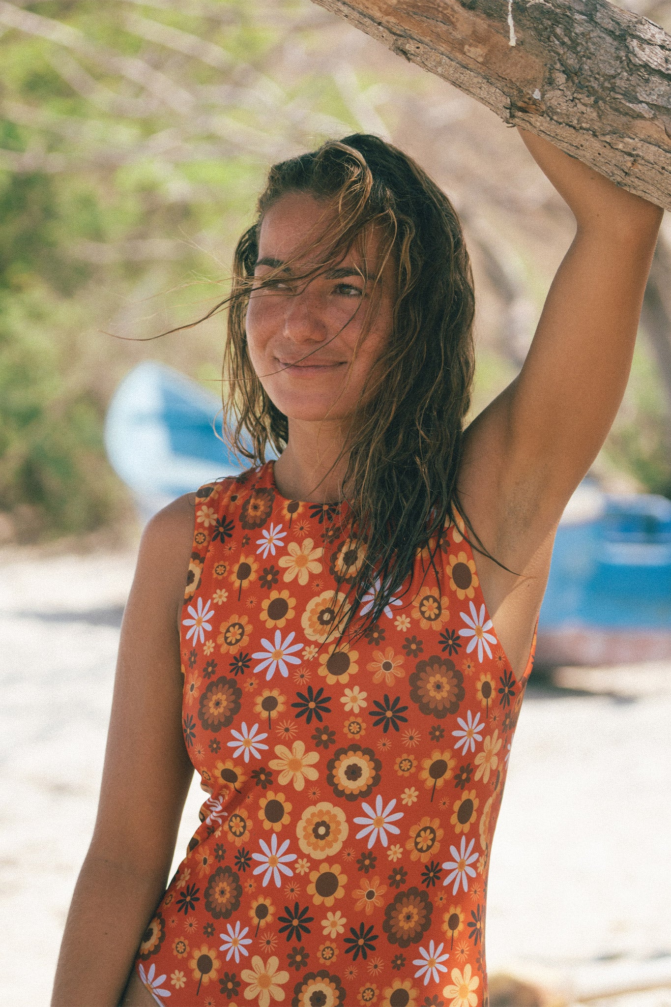 Brunette model posing next to a tree at the beach wearing the retro floral print surf suit