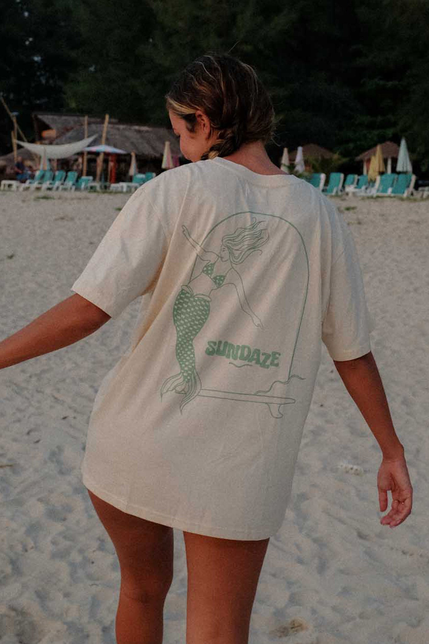 Model posing at the beach from the back, showing her t-shirt with mermaid illustration