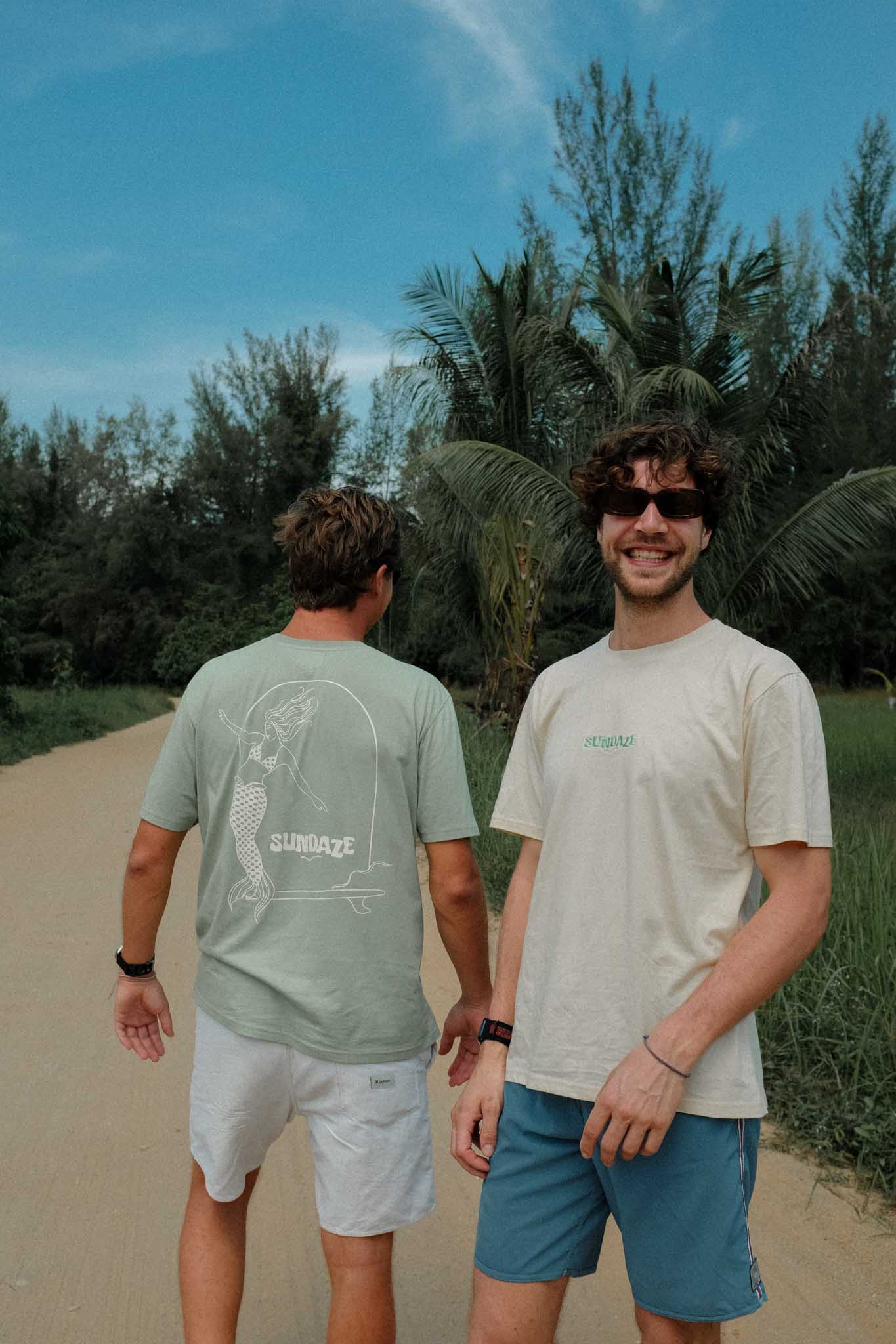 two boys posing in tropical lifestyle setting, smiling at the camera and both wearing a sundaze t-shirt