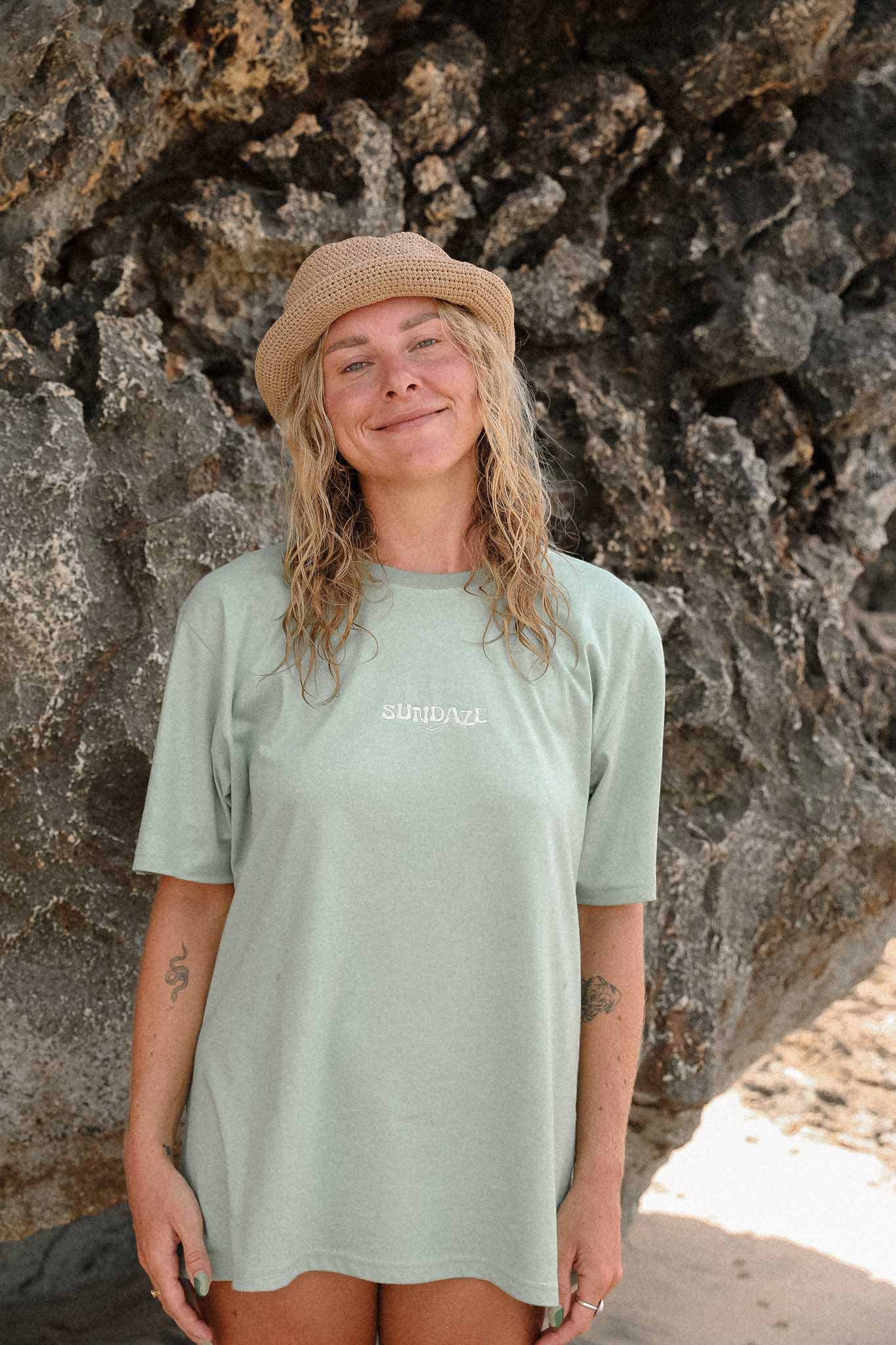 Woman posing from the front wearing a sage green t-shirt with sundaze logo embroidered on the front