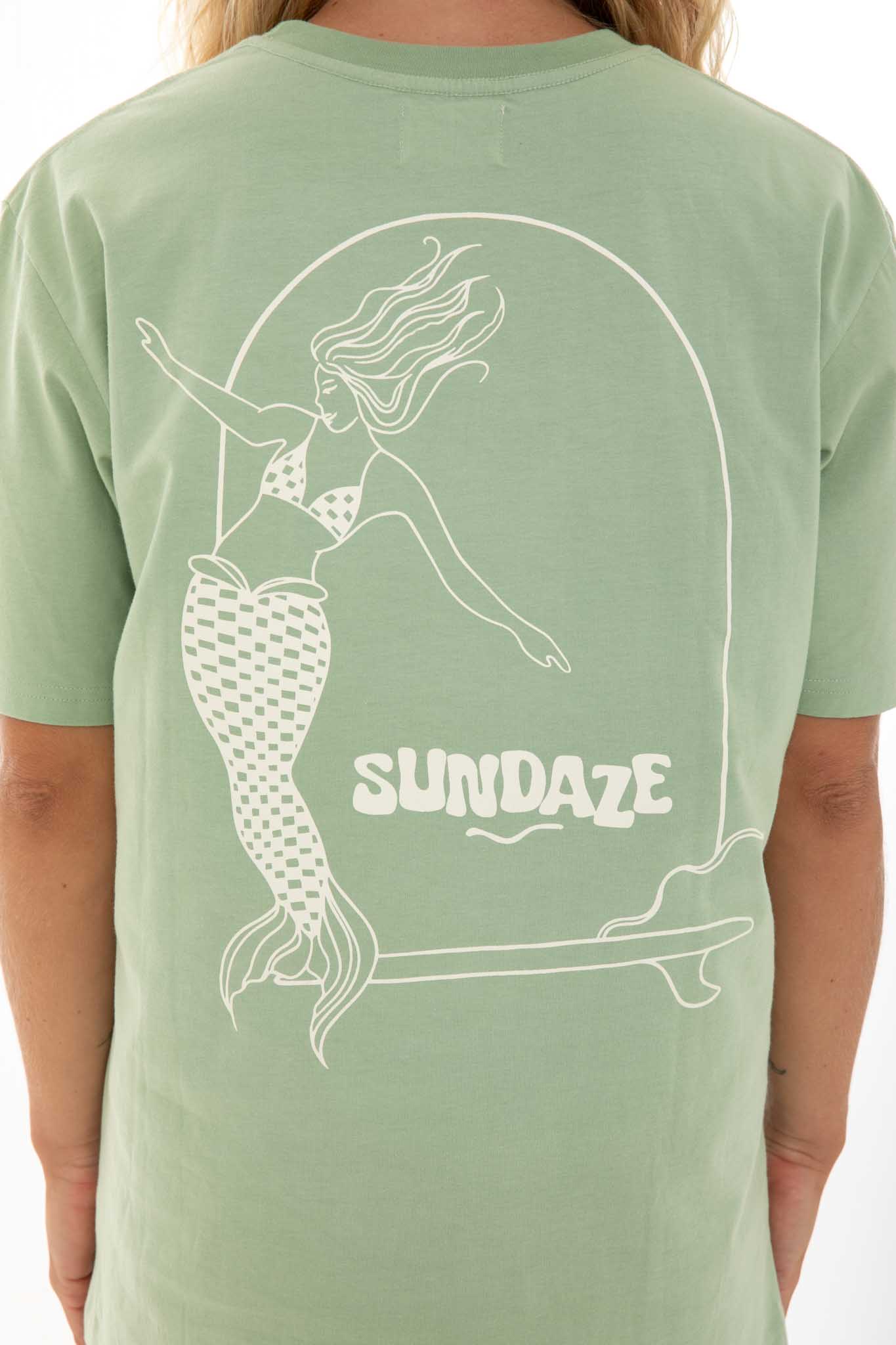 Woman posing, showing the back of her t-shirt wil an illustration of a mermaid on a surfboard