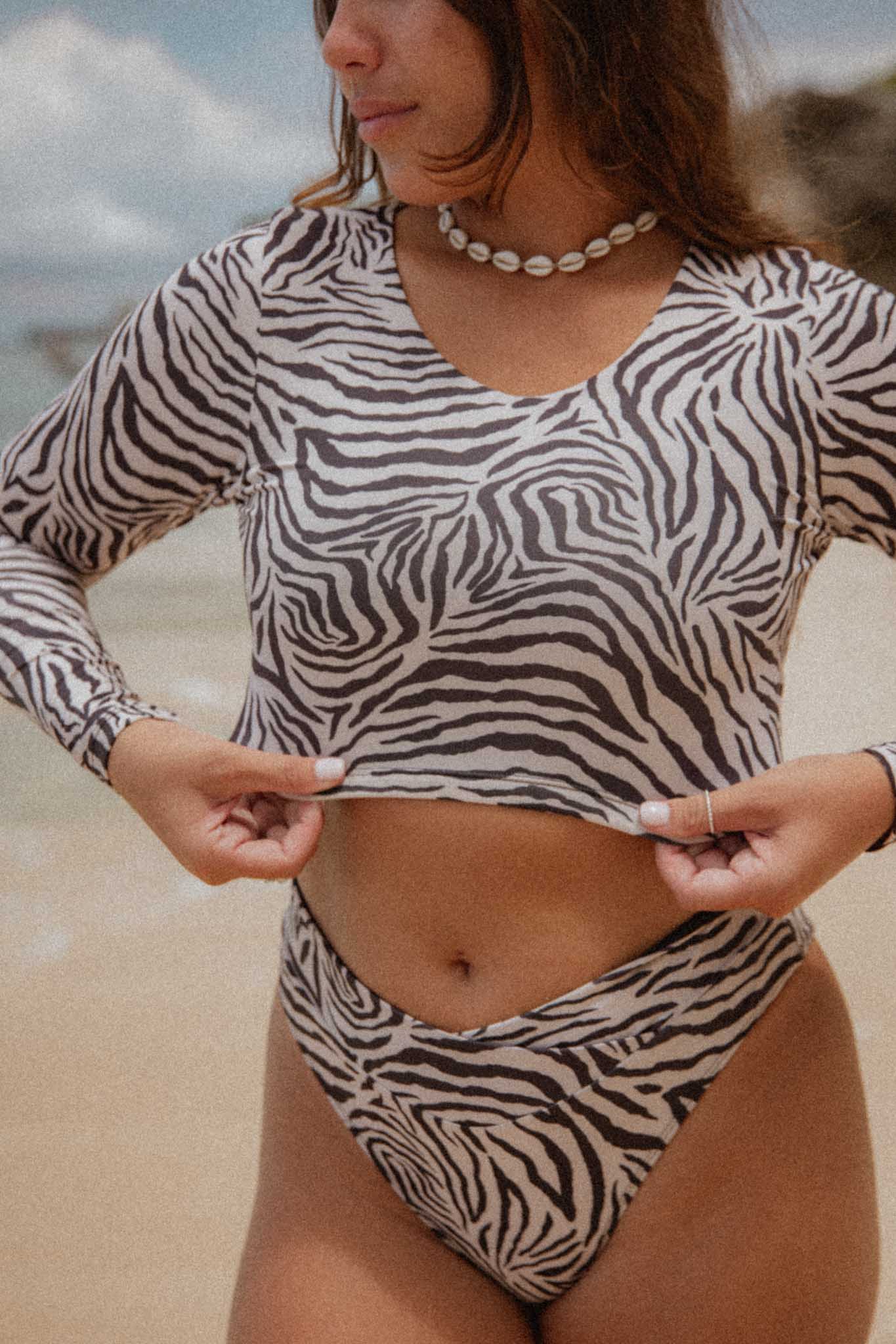 Close-up of a woman at the beach wearing the Nyoman set with Zebra print, pulling on the top