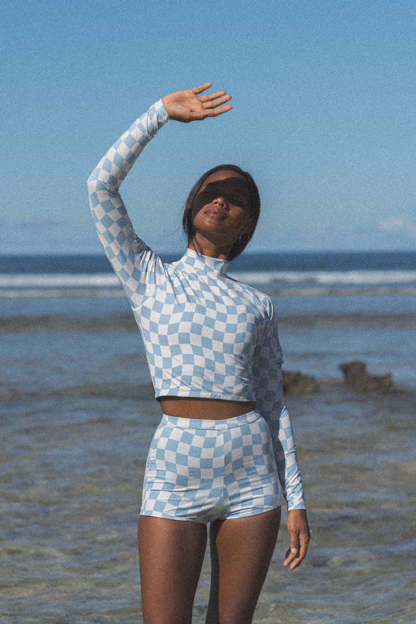 A model posing in the Putu Boy Short Bottom swimwear in a checkered pattern