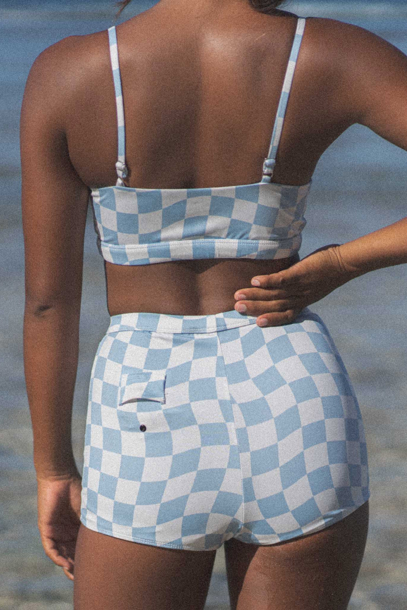 Model at the beach wearing the Putu boy bottoms in blue check print