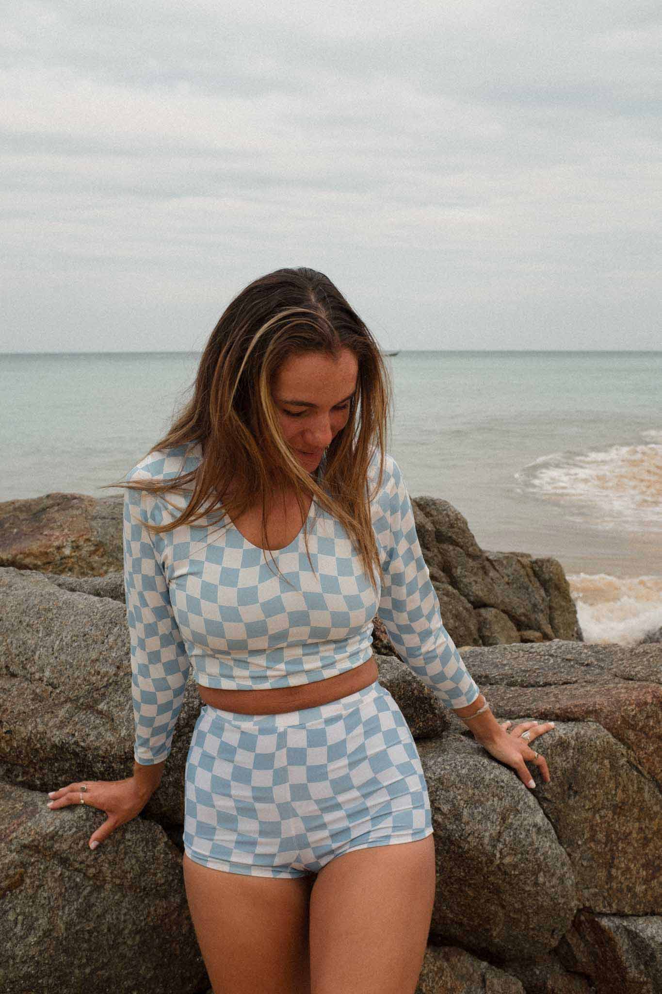 Model at the beach wearing the putu scoop neck top in blue check