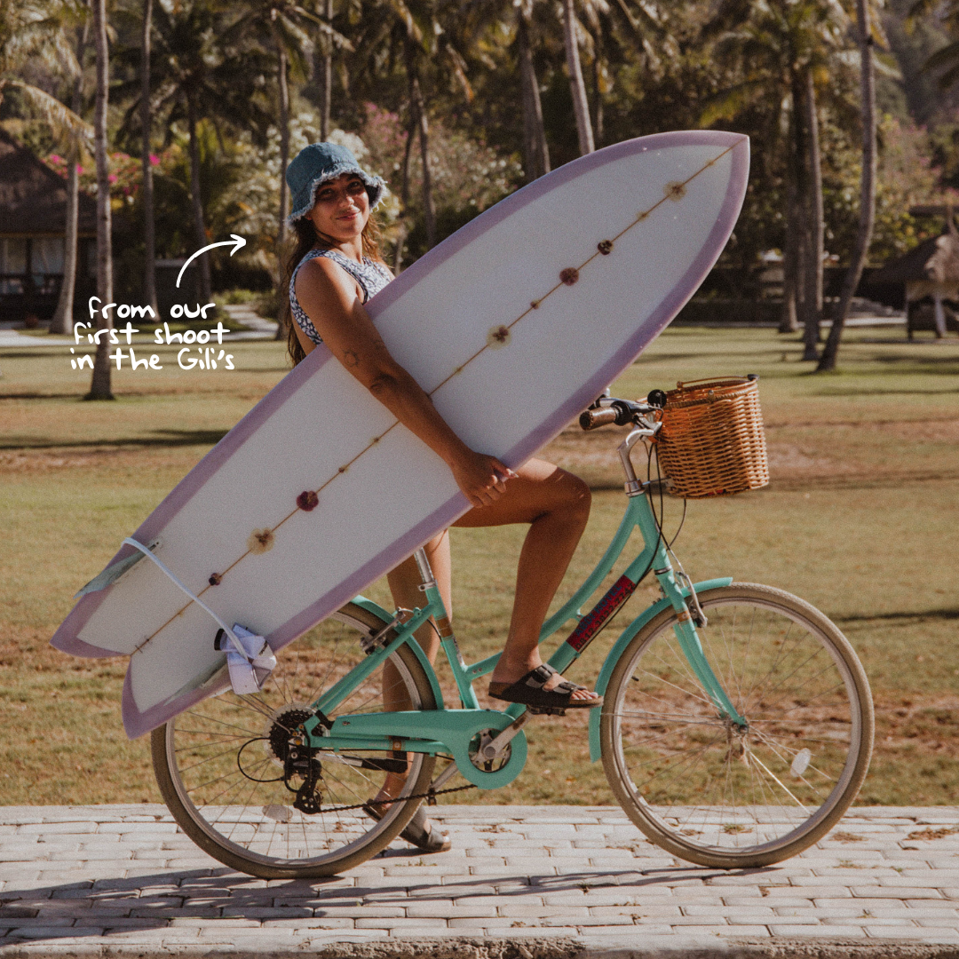 rebecca on a bicycle in gili with surfboard in hand