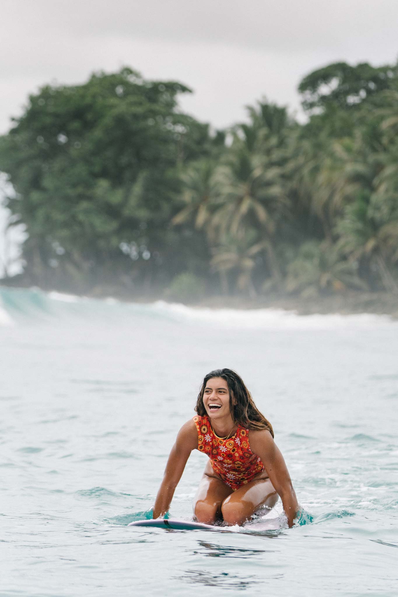 surfer sitting on her surfboard smiling and wearing the ketut surf suit in retro floral print