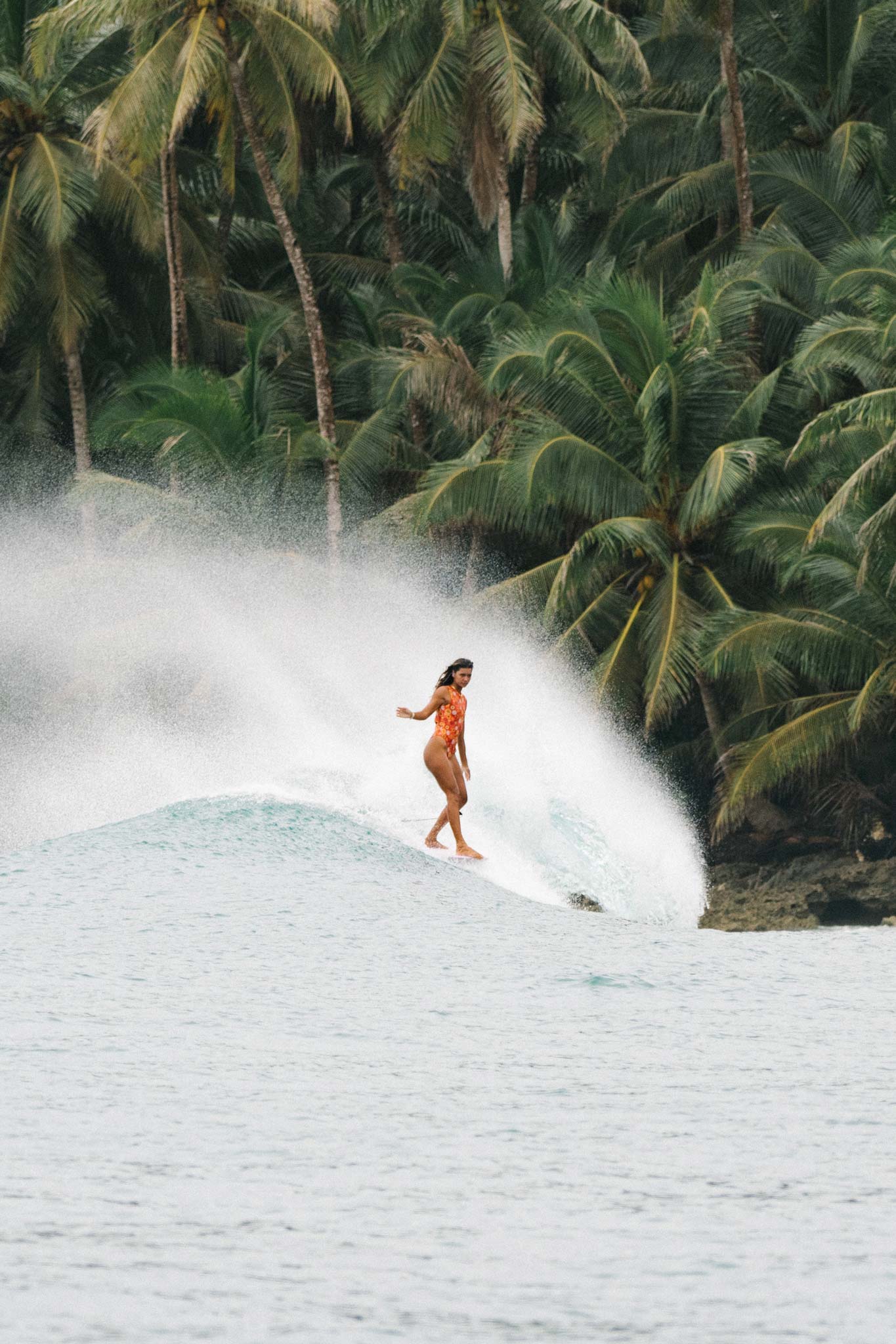 model surfing with a wave spraying behind her and palmtrees in the background