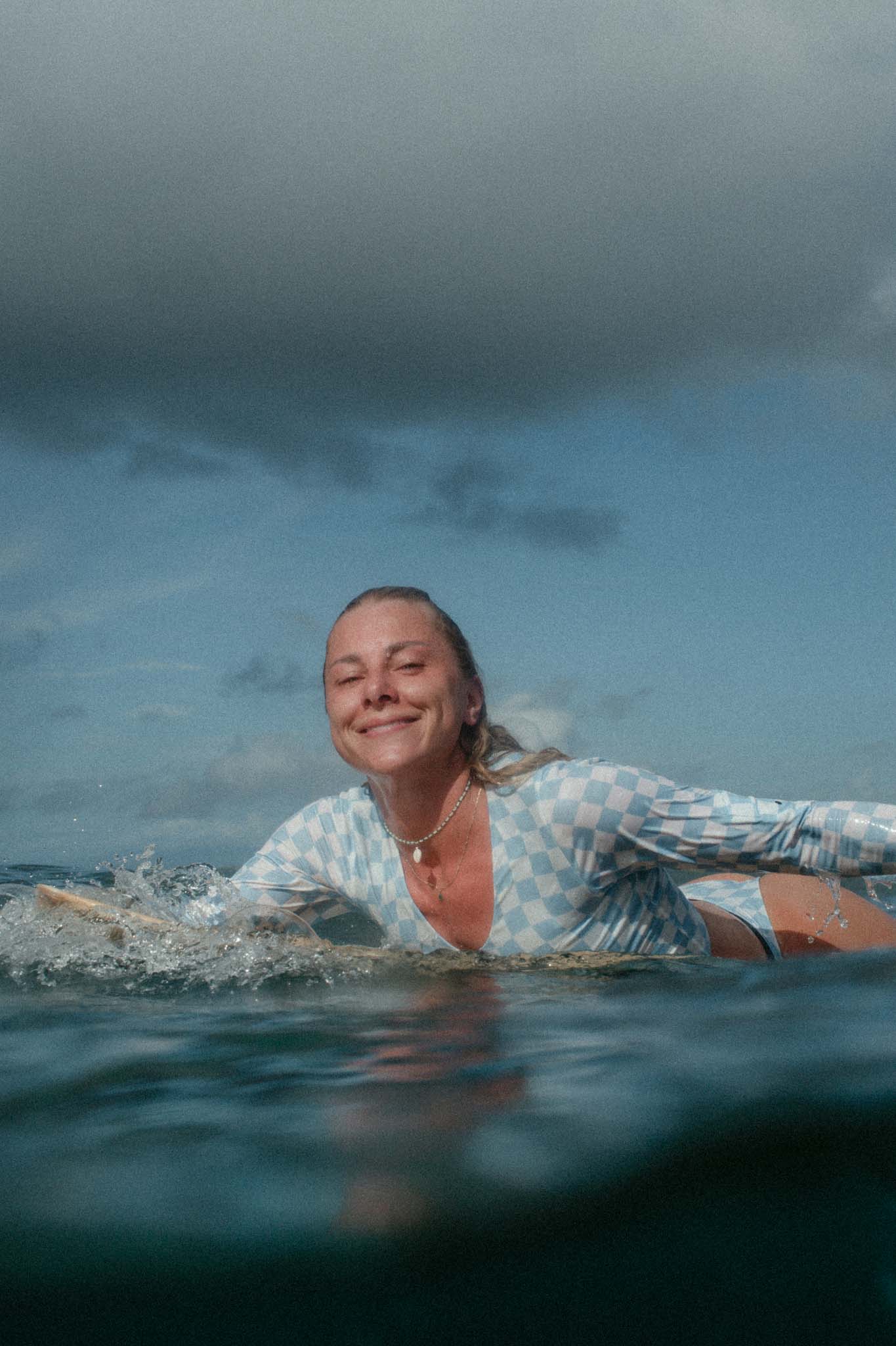 surfing paddling in the water smiling at the camera and wearing the blue check set